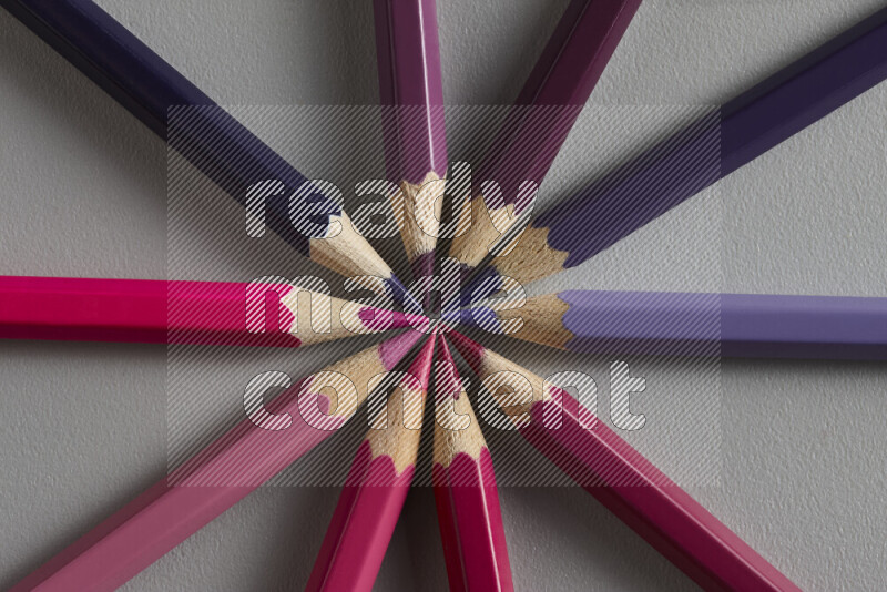 An arrangement of colored pencils in shades of pink and purple on grey background
