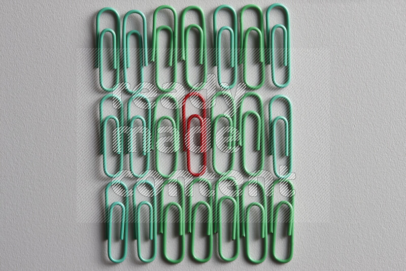 A red paperclip surrounded by bunch of green paperclips on grey background