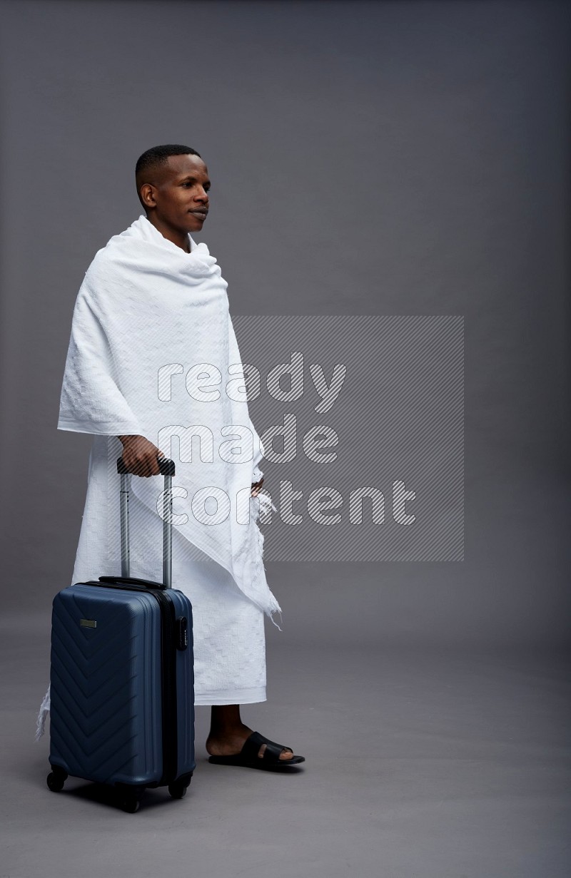 A man wearing Ehram Standing holding traveling bag on gray background