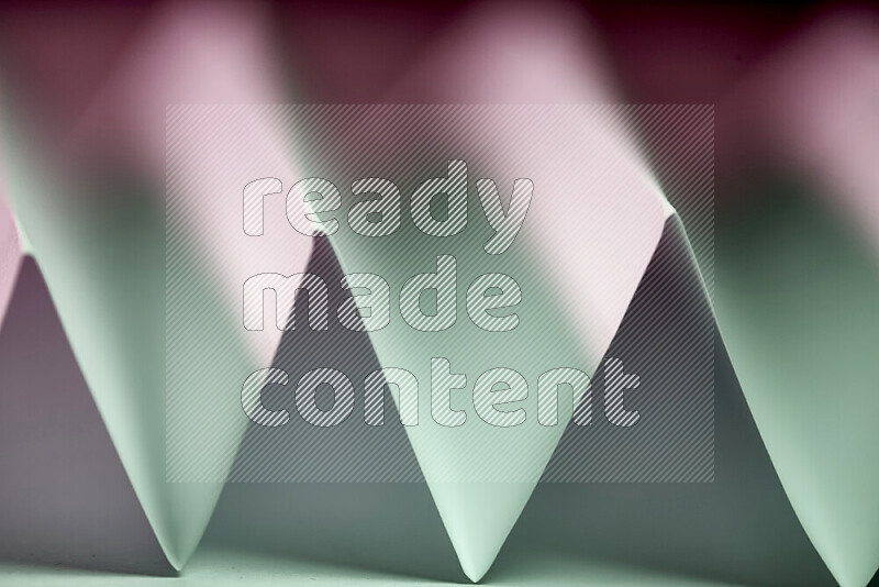 A close-up abstract image showing sharp geometric paper folds in green and pink gradients