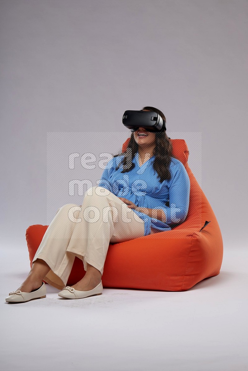 A woman sitting on an orange beanbag and gaming with VR