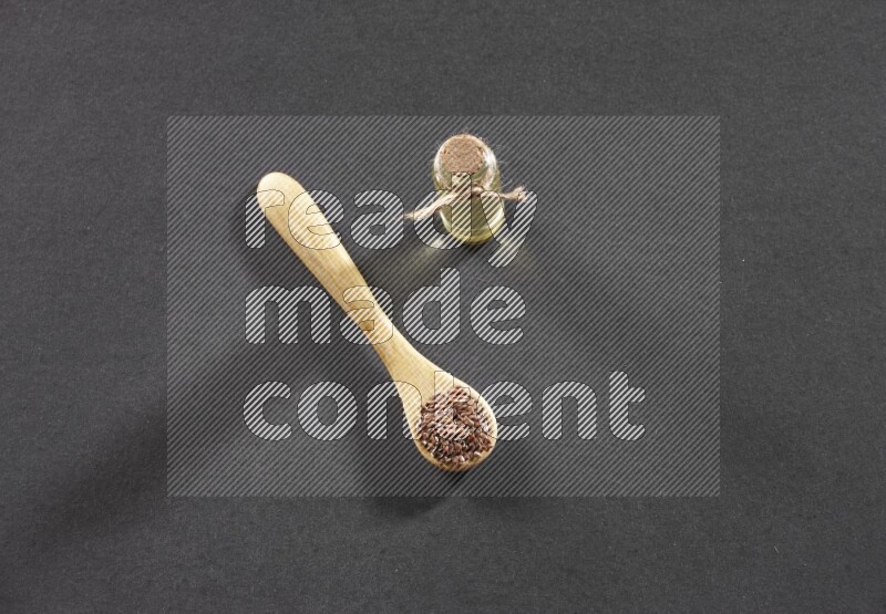 وعاء خشبي ممتلئ بحبوب بذر الكتان مع زجاجة من زيت بذر الكتان علي خلفية سوداء