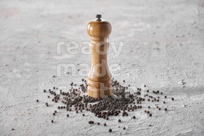 A wooden grinder with black pepper beads on a textured white flooring