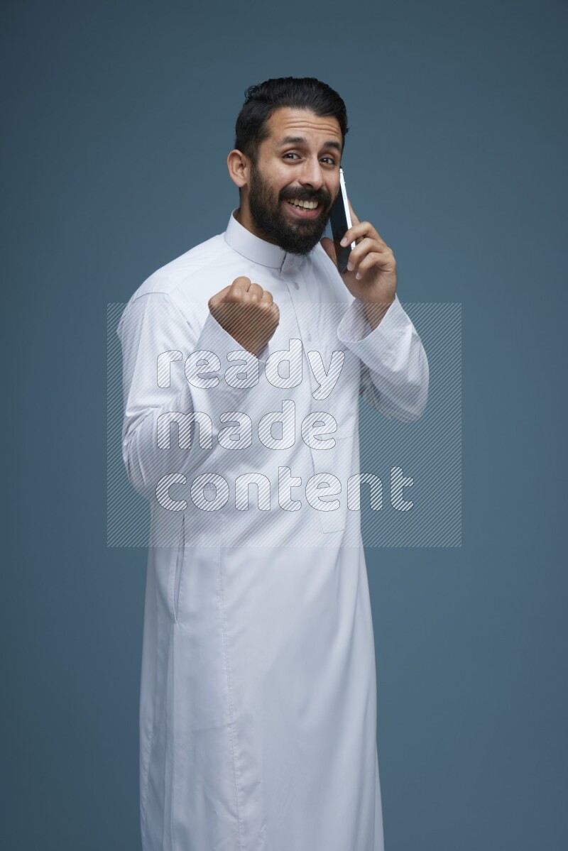 A man having a call on a blue background wearing Saudi Thob