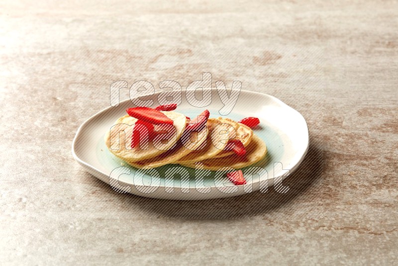 Five stacked strawberry mini pancakes in a bicolor plate on beige background