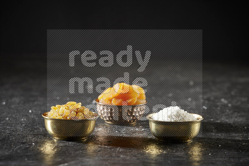 Dried fruits in metal bowls in a dark setup