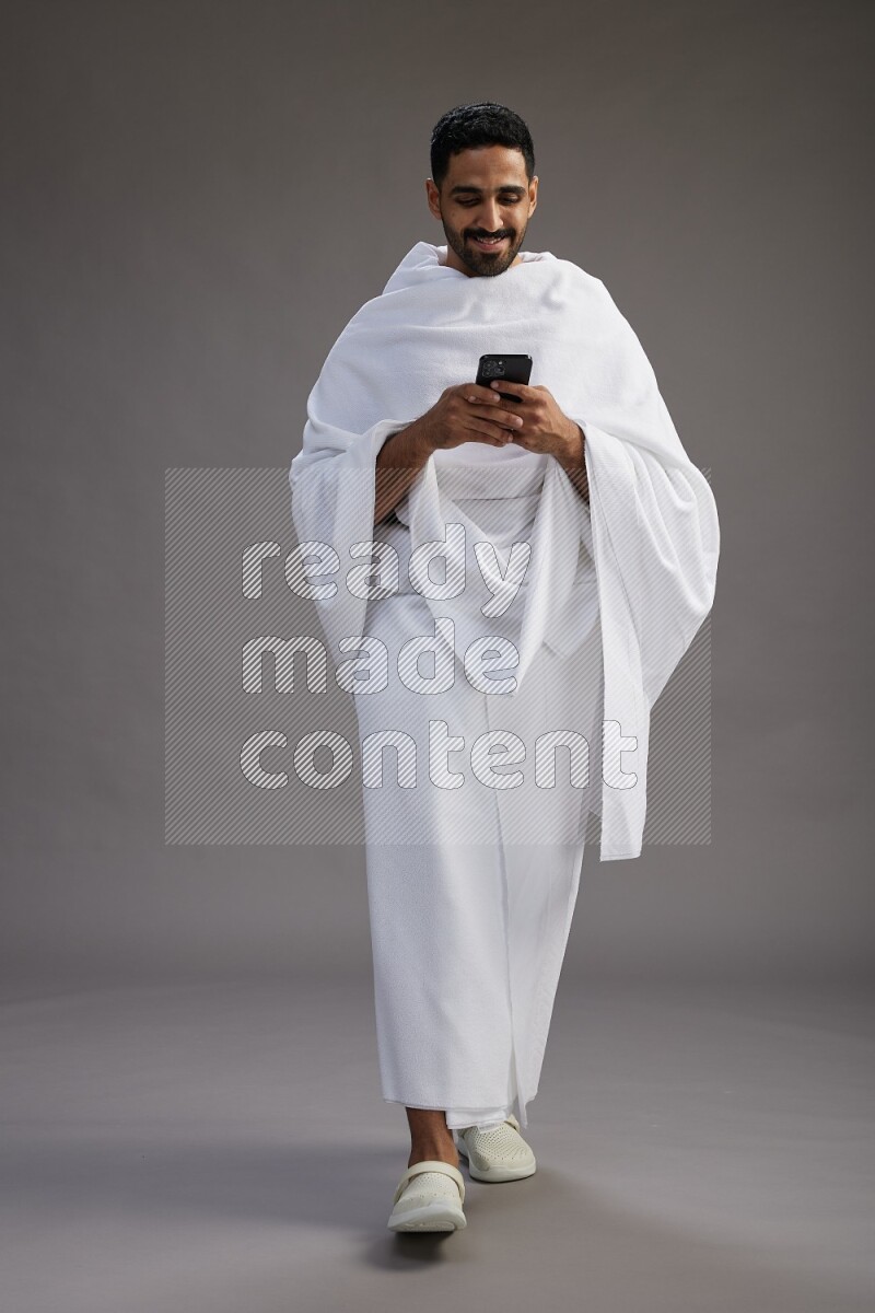 A man wearing Ehram Standing texting on phone on gray background