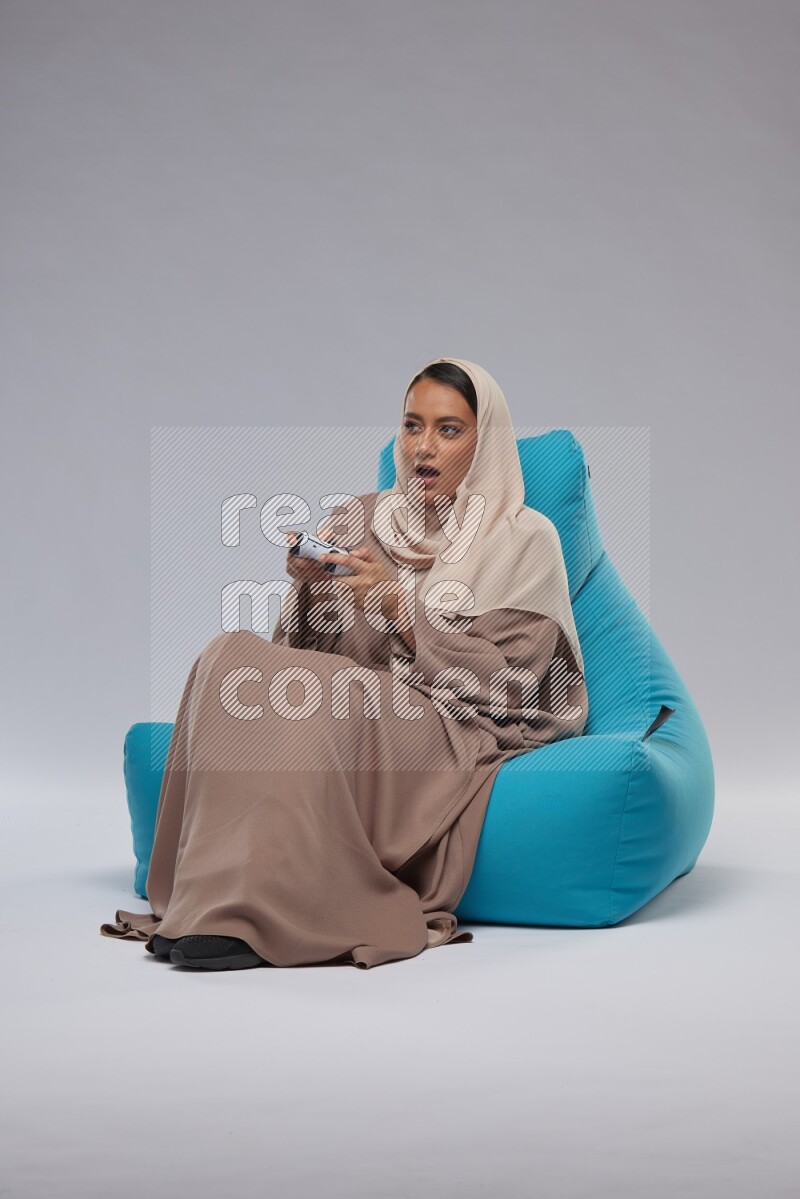 A Saudi woman sitting on a blue beanbag and gaming with joystick