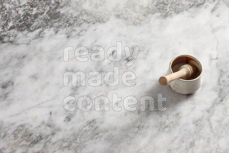 Beige Pottery Bowl with wooden honey handle in it, on grey marble flooring, 65 degree angle