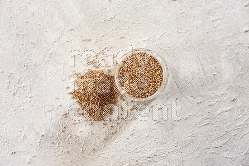 A glass jar full of mustard seeds and more seeds spread on a textured white flooring in different angles