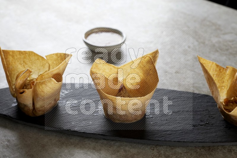 wonton cups with soy sauce ramkin on oval slate on grey textured counter top