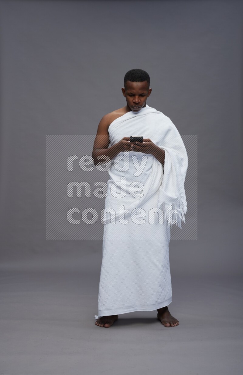 A man wearing Ehram Standing texting on phone on gray background