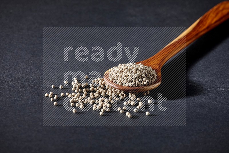 A wooden ladle full of white pepper beads on black flooring