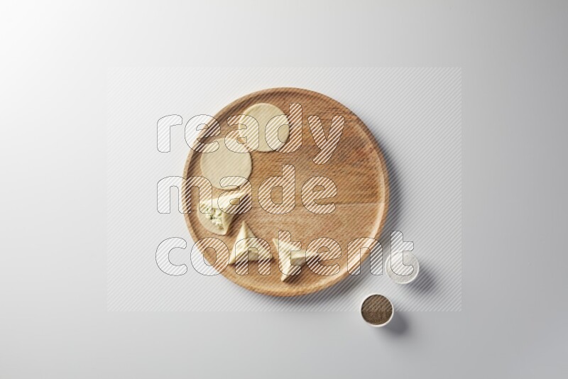 two closed sambosas and one open sambosa filled with cheese while salt, and black pepper aside in a wooden dish on a white background