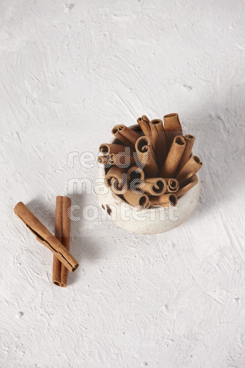Cinnamon sticks in a beige bowl on a white background