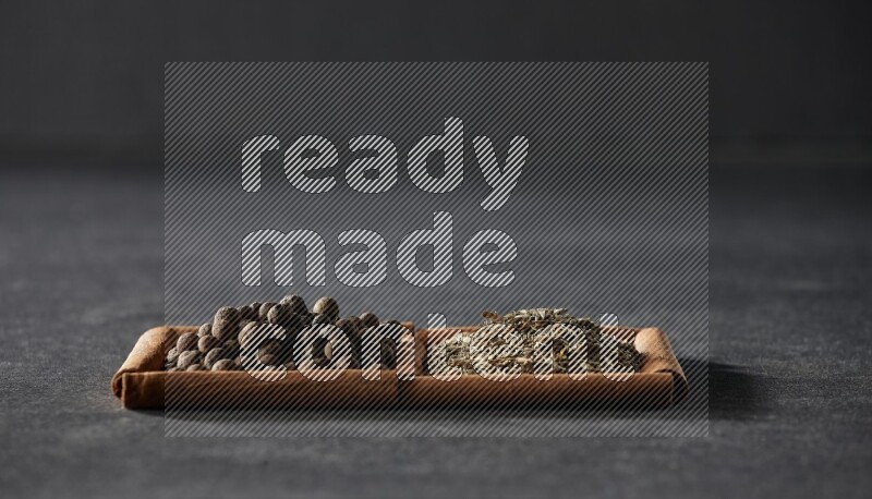 مربعان من أعواد القرفة ممتلئان بحبوب الكمون وحبوب بهار الفلفل الحلو علي خلفية سوداء