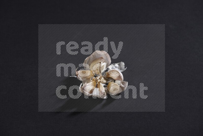 A cracked garlic bulb showing the cloves inside it on a black flooring