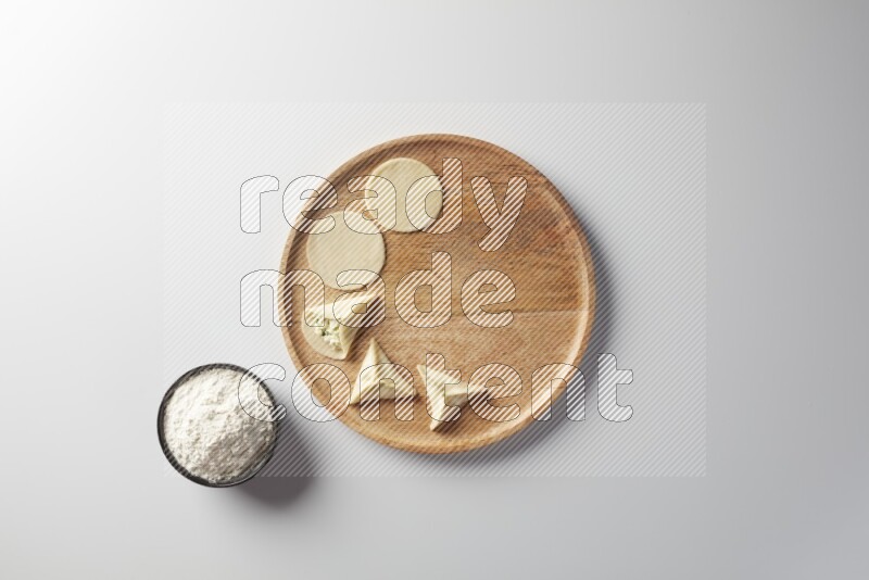 two closed sambosas and one open sambosa filled with cheese while flour aside in a wooden dish on a white background