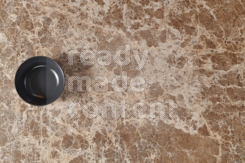 A black ceramic bowl on beige marble background