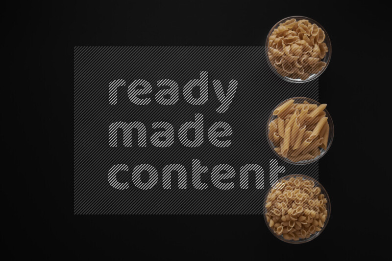 Different pasta types in 3 glass bowls on black background