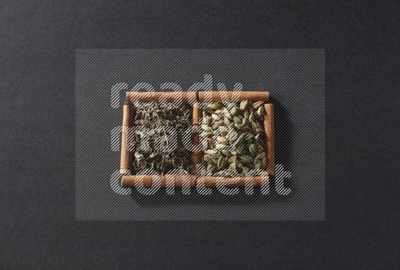 مربعان من أعواد القرفة ممتلئان بحبوب الهيل والريحان المجفف علي خلفية سوداء