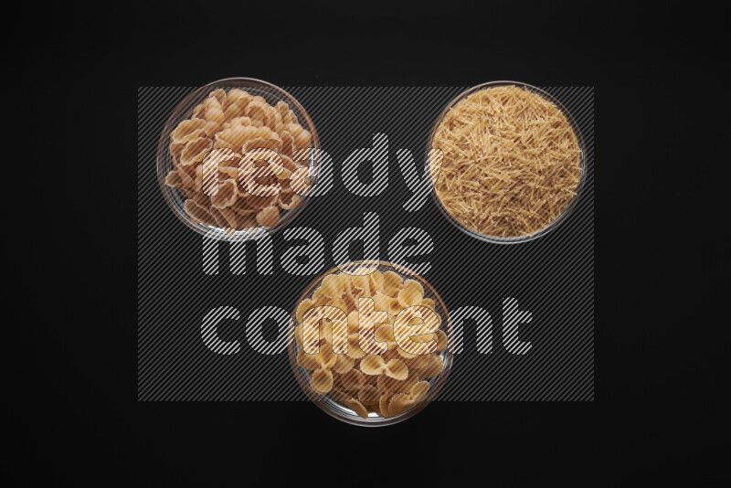 Different pasta types in glass bowls on black background