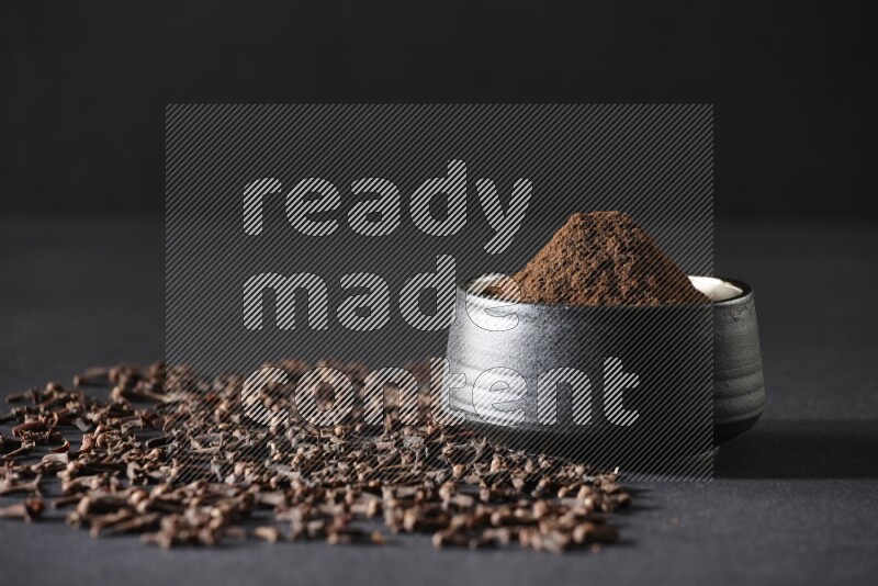 وعاء فخاري أسود ممتلئ ببودرة القرنفل وحبوب القرنفل على خلفية سوداء