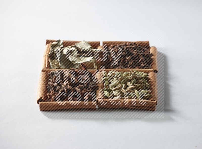 4 مربعات من أعواد القرفة ممتلئة بالهيل واليانسون والقرنفل وأوراق الغار على أرضية بيضاء