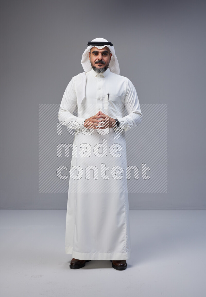 Saudi man Wearing Thob and white Shomag standing interacting with the camera on Gray background