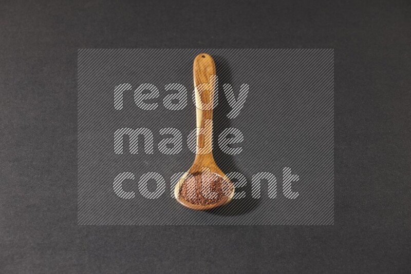A wooden ladle full of garden cress seeds on a black flooring