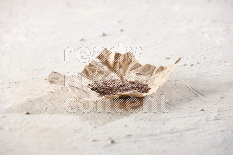 A crumpled piece of paper full of flax seeds on a textured white flooring
