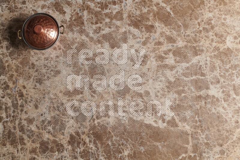 A small copper pot on beige marble background