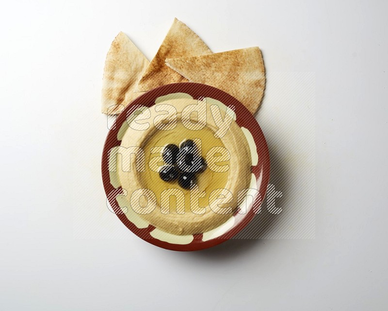 Hummus in a traditional plate garnished with black olives on a white background