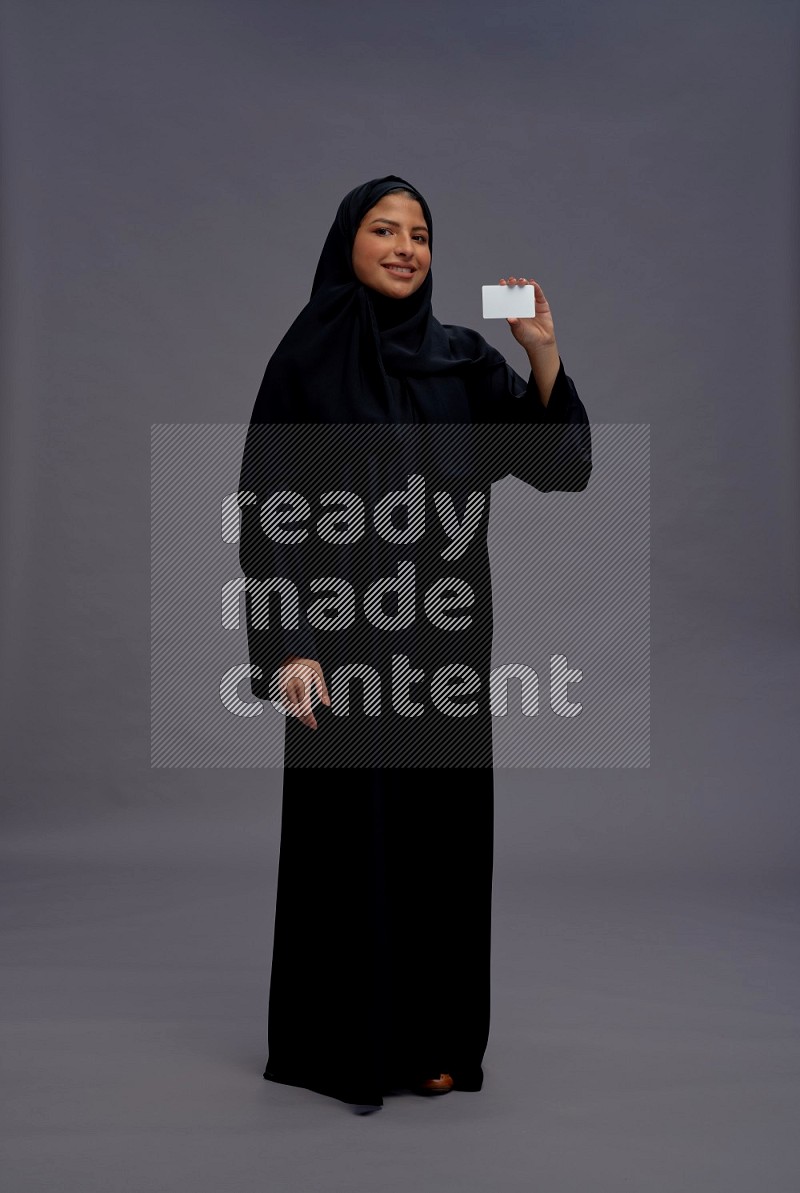 Saudi woman wearing Abaya standing holding ATM card on gray background