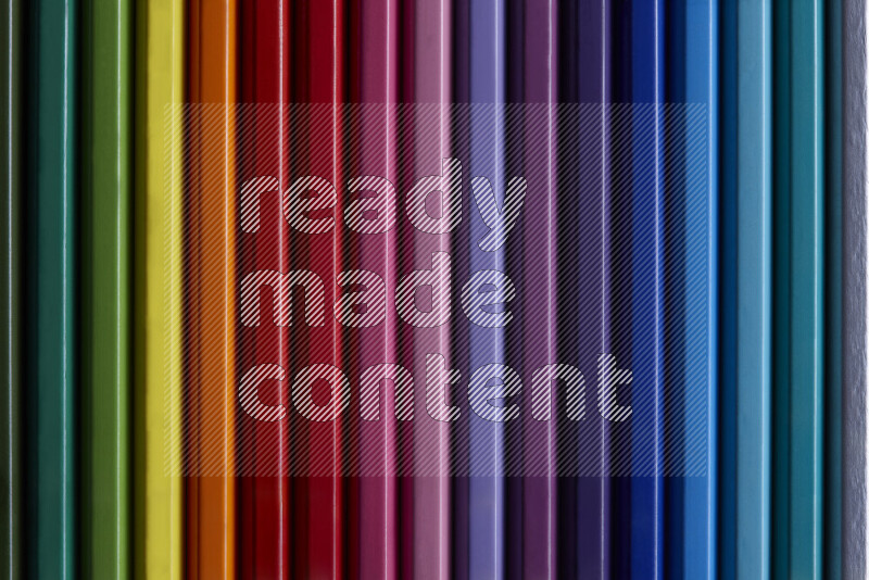 A collection of colored pencils arranged showcasing a gradient of different hues on grey background