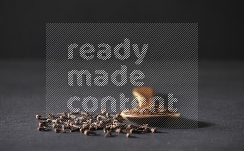 مغرفة خشبية ممتلئة ببودرة القرنفل مع بعض حبوب القرنفل الكاملة حولها على خلفية سوداء