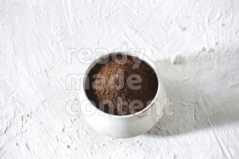 A beige ceramic bowl full of cloves powder on a white flooring