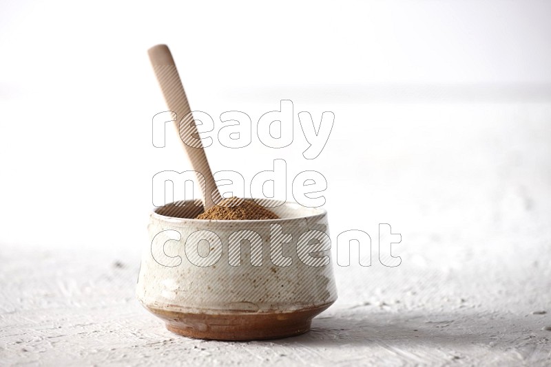 Ceramic beige bowl full of cinnamon powder with a wooden spoon on a textured white background