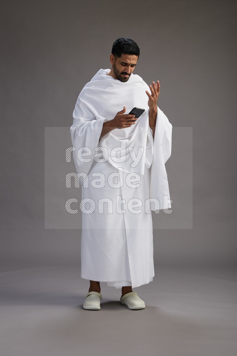 A man wearing Ehram Standing texting on phone on gray background