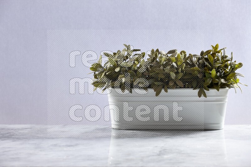 Multiple green artificial plants in white pot on grey marble background