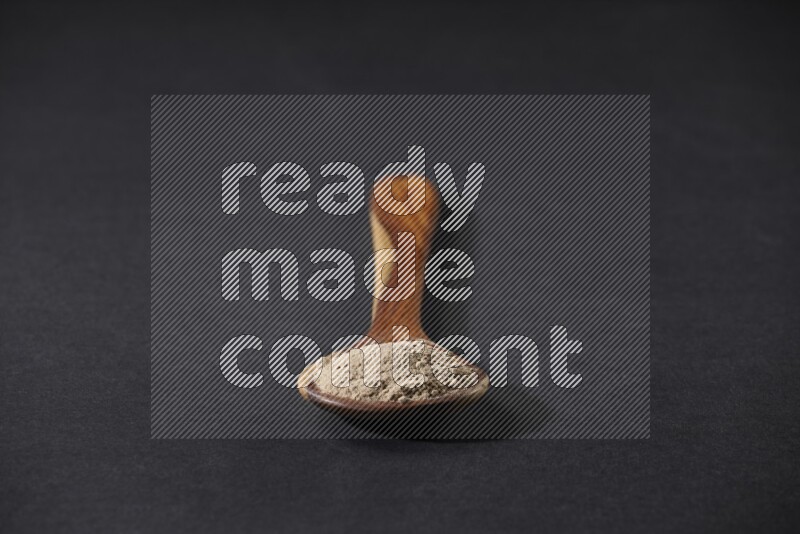 ملعقة خشبية كبيرة مليئة ببودرة الثوم على خلفية سوداء