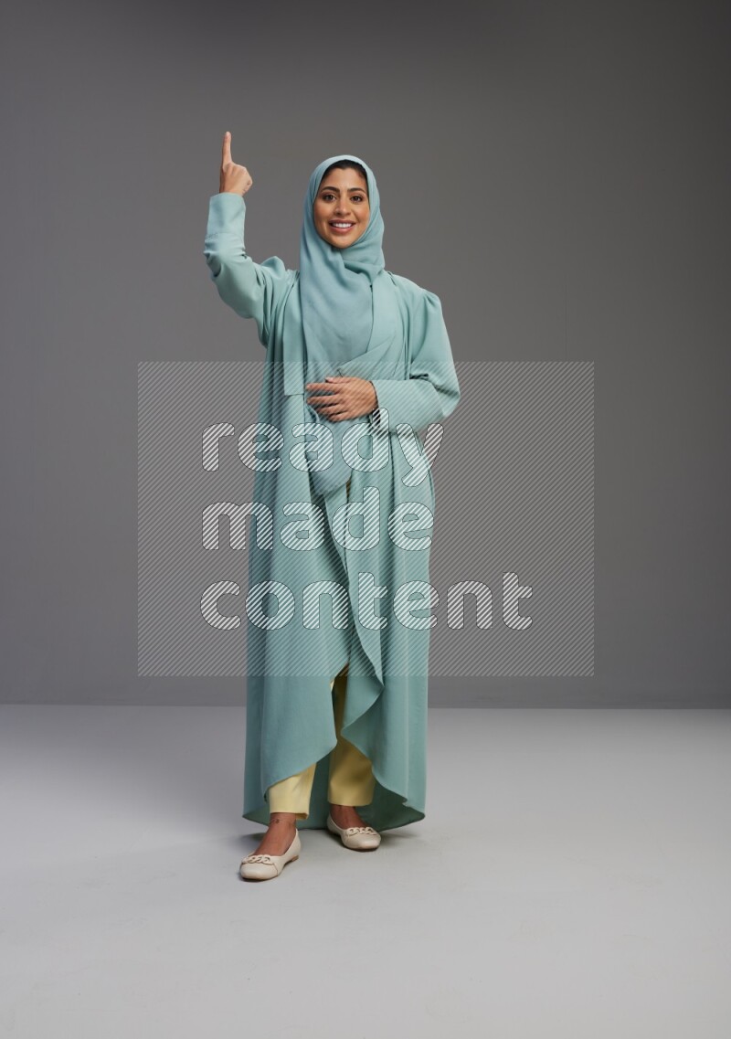 Saudi Woman wearing Abaya standing interacting with the camera on Gray background