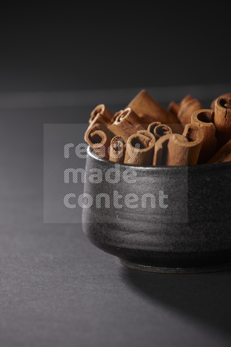 Cinnamon sticks in a black bowl on a black background in different angles