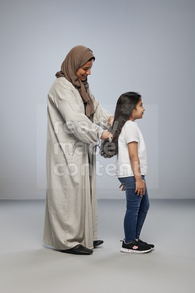 Mom standing styling hair for her daughter on gray background