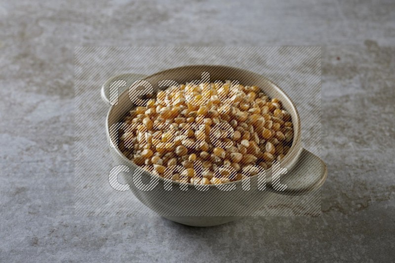 corn kernel in a off-white handheld ceramic bowl on a grey textured countertop
