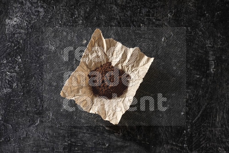 Cloves powder in crumpled piece of paper on a textured black flooring