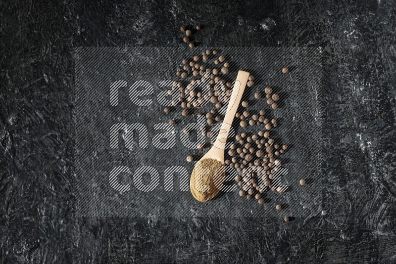 ملاعق خشبية ممتلئة ببودرة بهار الفلفل الحلو وحبوبه بجانبها على خلفية سوداء