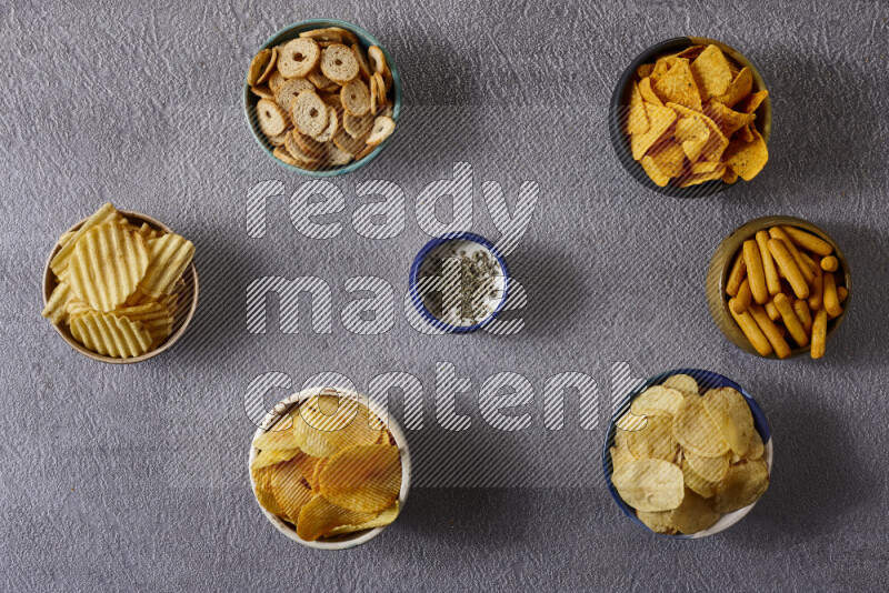 Assorted snacks in pottery bowls on grey background