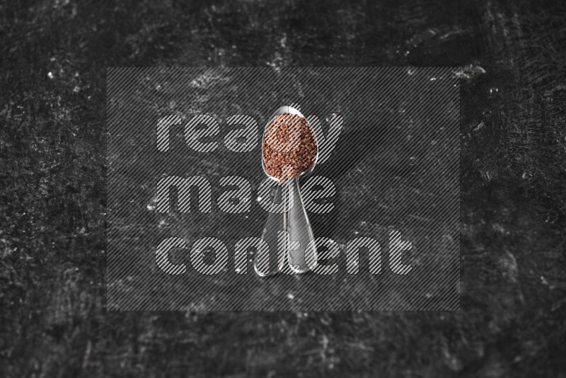 2 metal spoons full of garden cress seeds on a textured black flooring