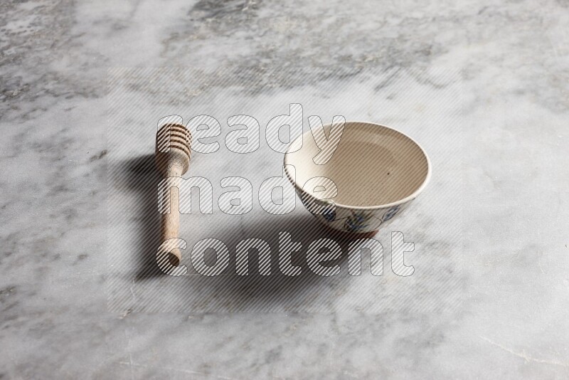 Decorative pottery bowl with wooden honey dipper on the side on grey marble background